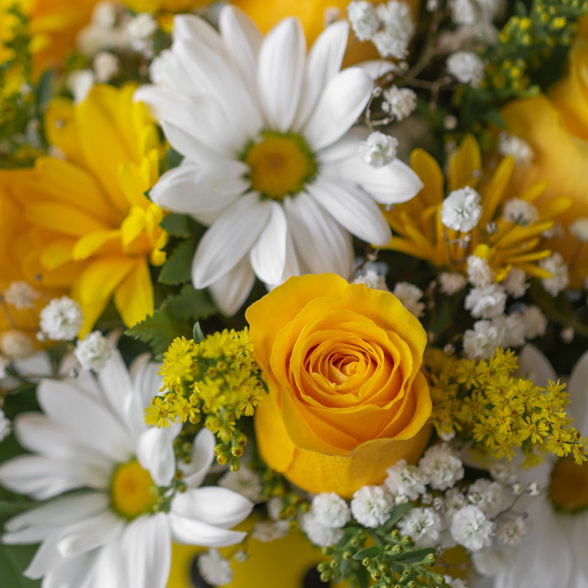 White and yellow daisies with roses, peppered with baby's breath and greens in a yellow smiley-face mug