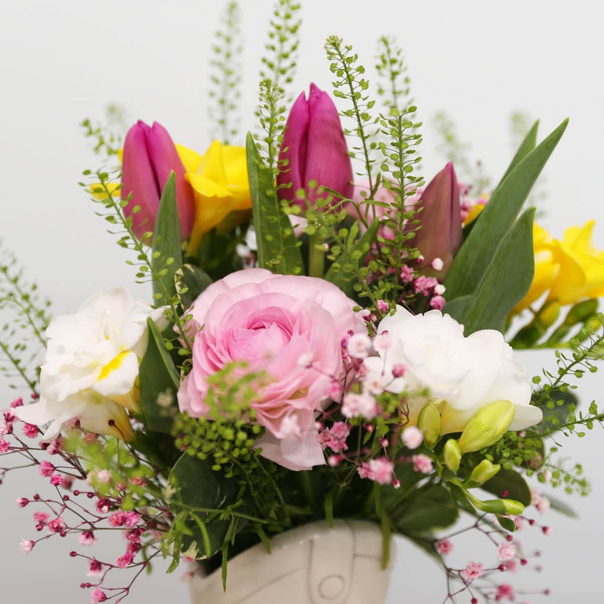 Mother's Day floral arrangement with tulips, ranunculus, freesias, and lisianthus in a ceramic boot vase