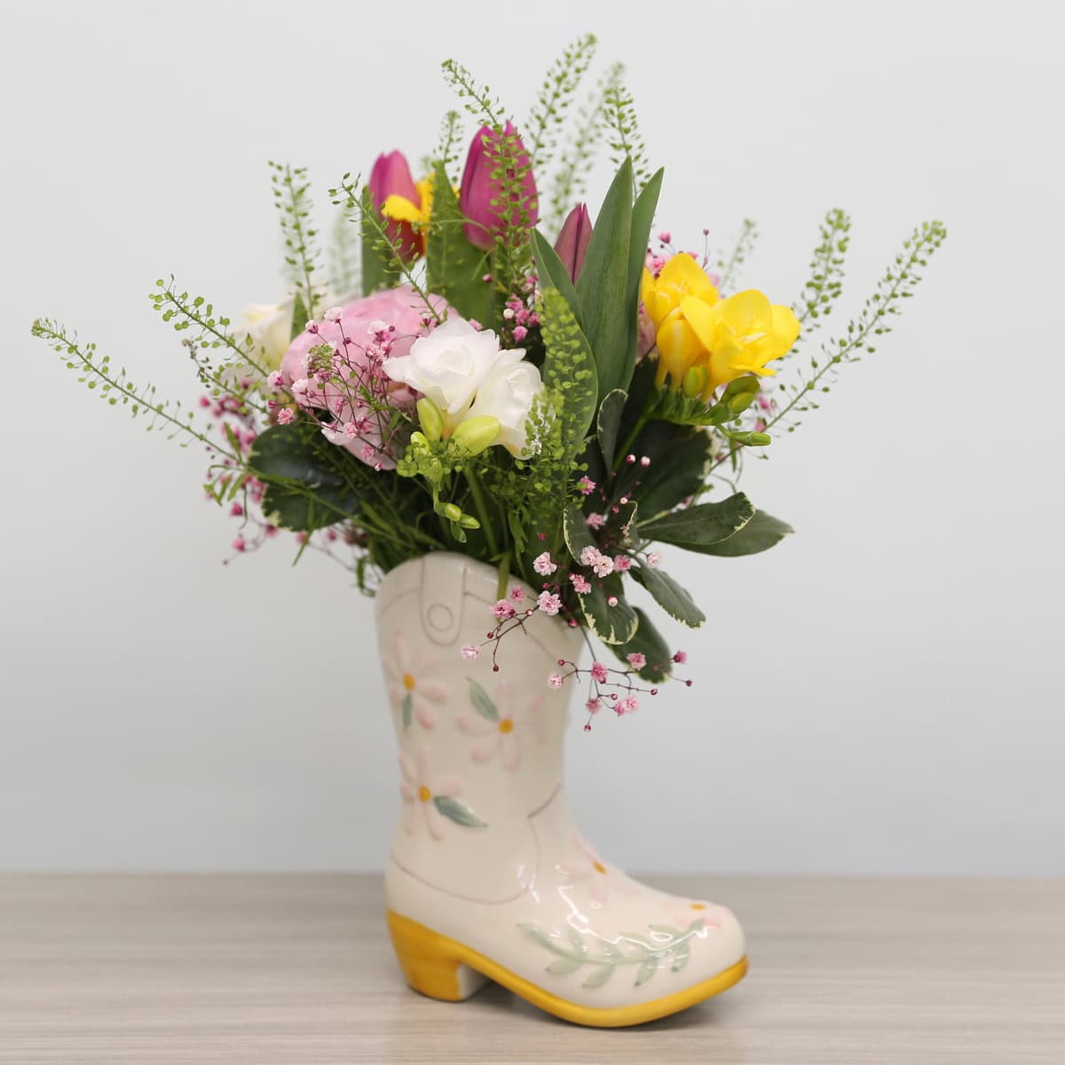 "Mother's Day floral arrangement with tulips, ranunculus, freesias, and lisianthus in a ceramic boot vase"