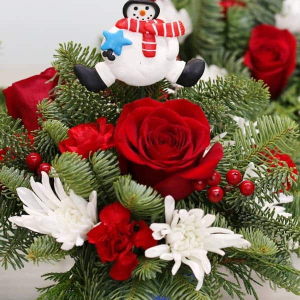 Arrangement de Noël Mini Sweets avec roses rouges, chrysanthèmes blancs, verdures et baies dans un pot rayé avec décoration canne de Noël.
