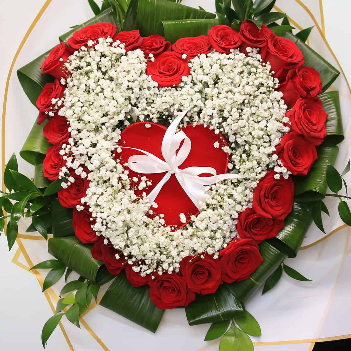 Heart-shaped bouquet made of 24 red roses framed with baby’s breath and greenery