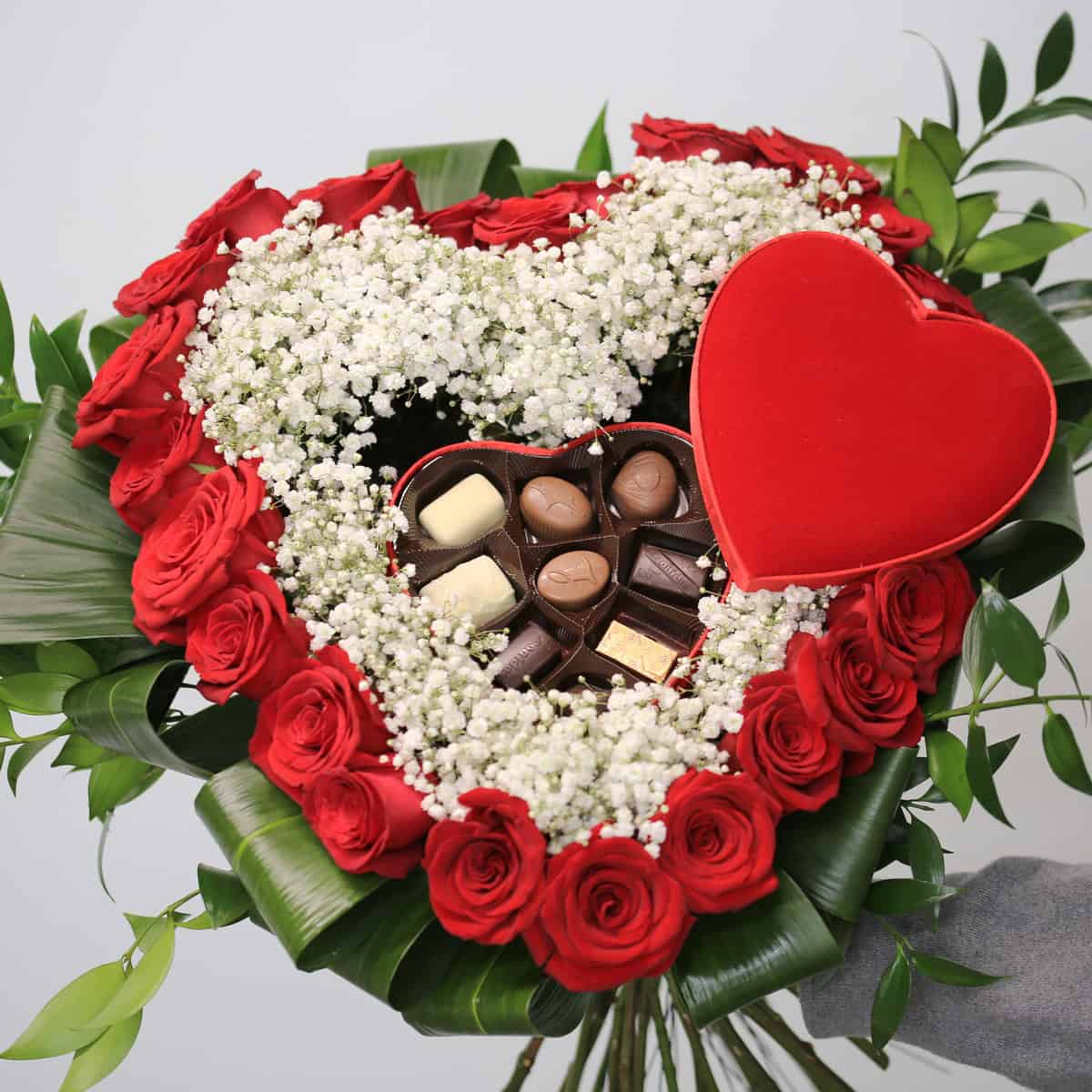 Heart-shaped bouquet of 24 red roses with baby’s breath and Leonidas chocolates in the center.