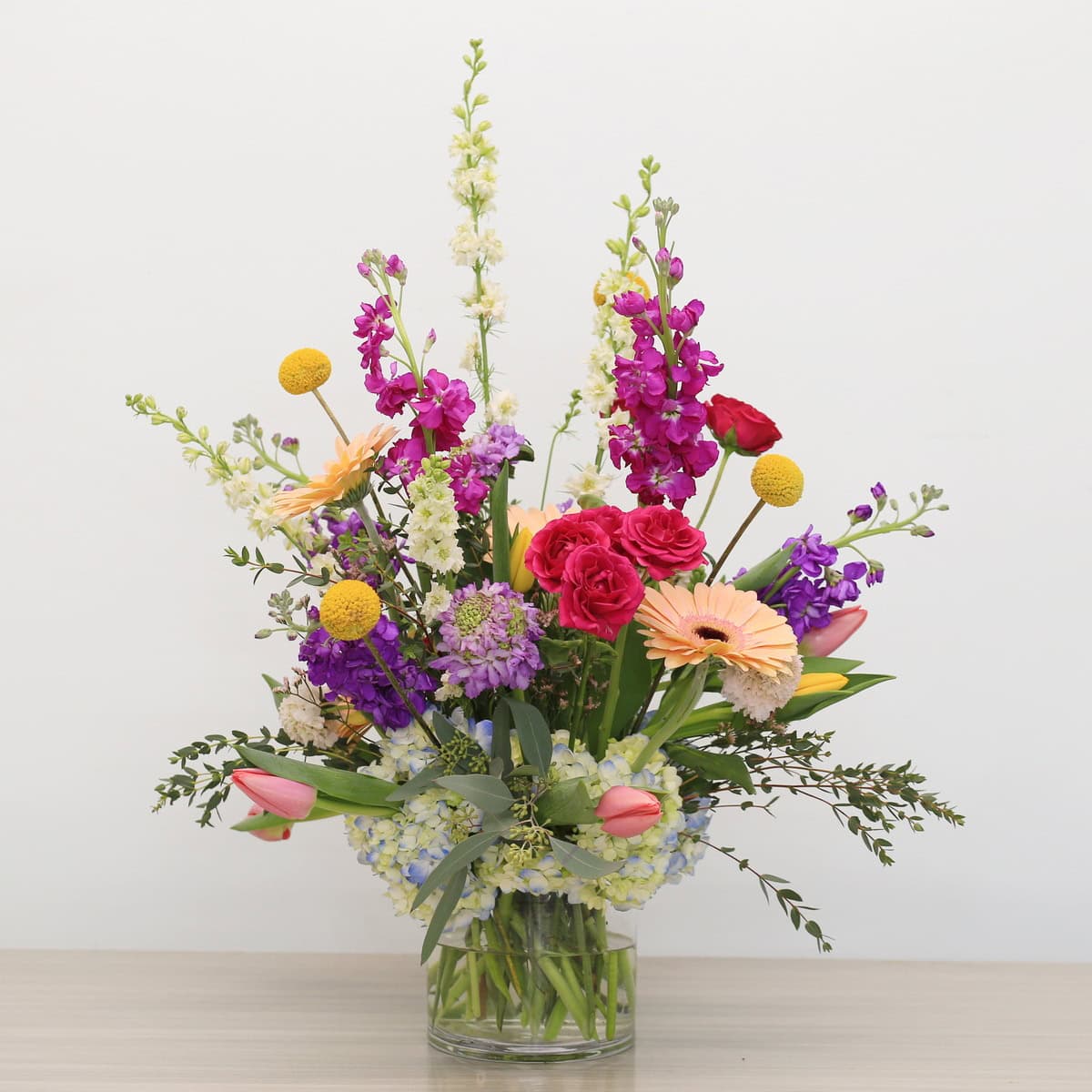 Field of Harmony modern floral arrangement with hydrangea base, roses, tulips, gerbera and stock in a clear glass vase.