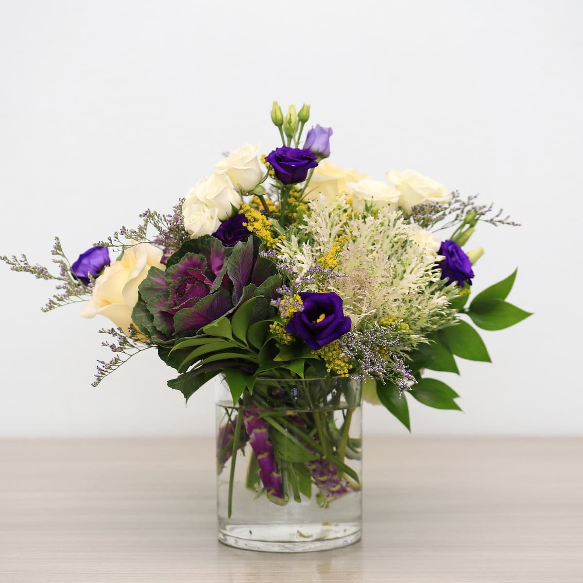 Violet Embrace floral arrangement with decorative kale, white roses, purple lisianthus, solidago in an etched Le Bouquet glass vase.