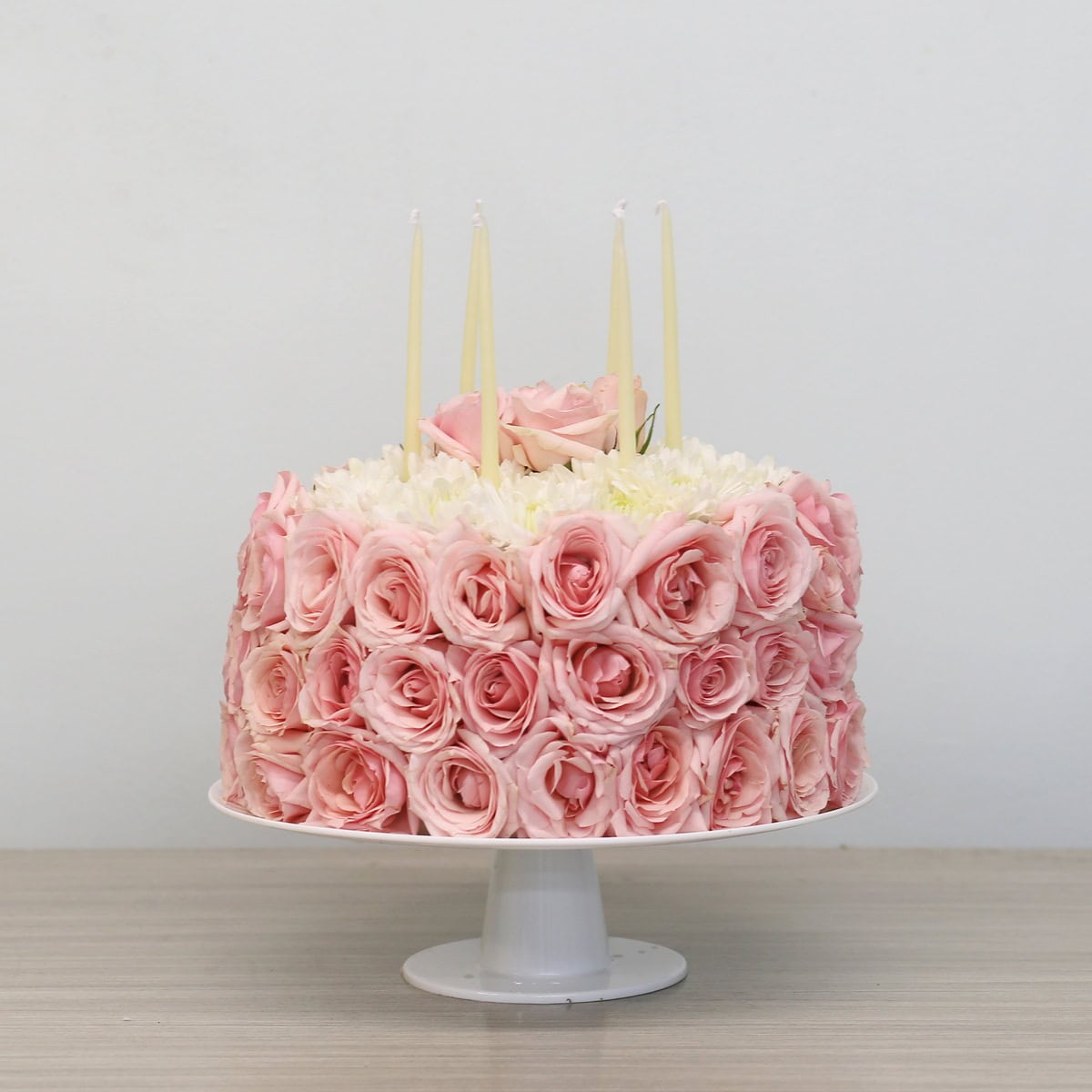 Birthday floral cake made of pink roses with candles on stand